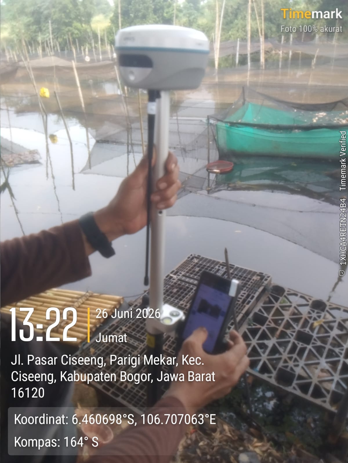 Surveyor holding an APEKS RTK GNSS receiver over an aquaculture fish pond in Bogor, West Java, Indonesia
