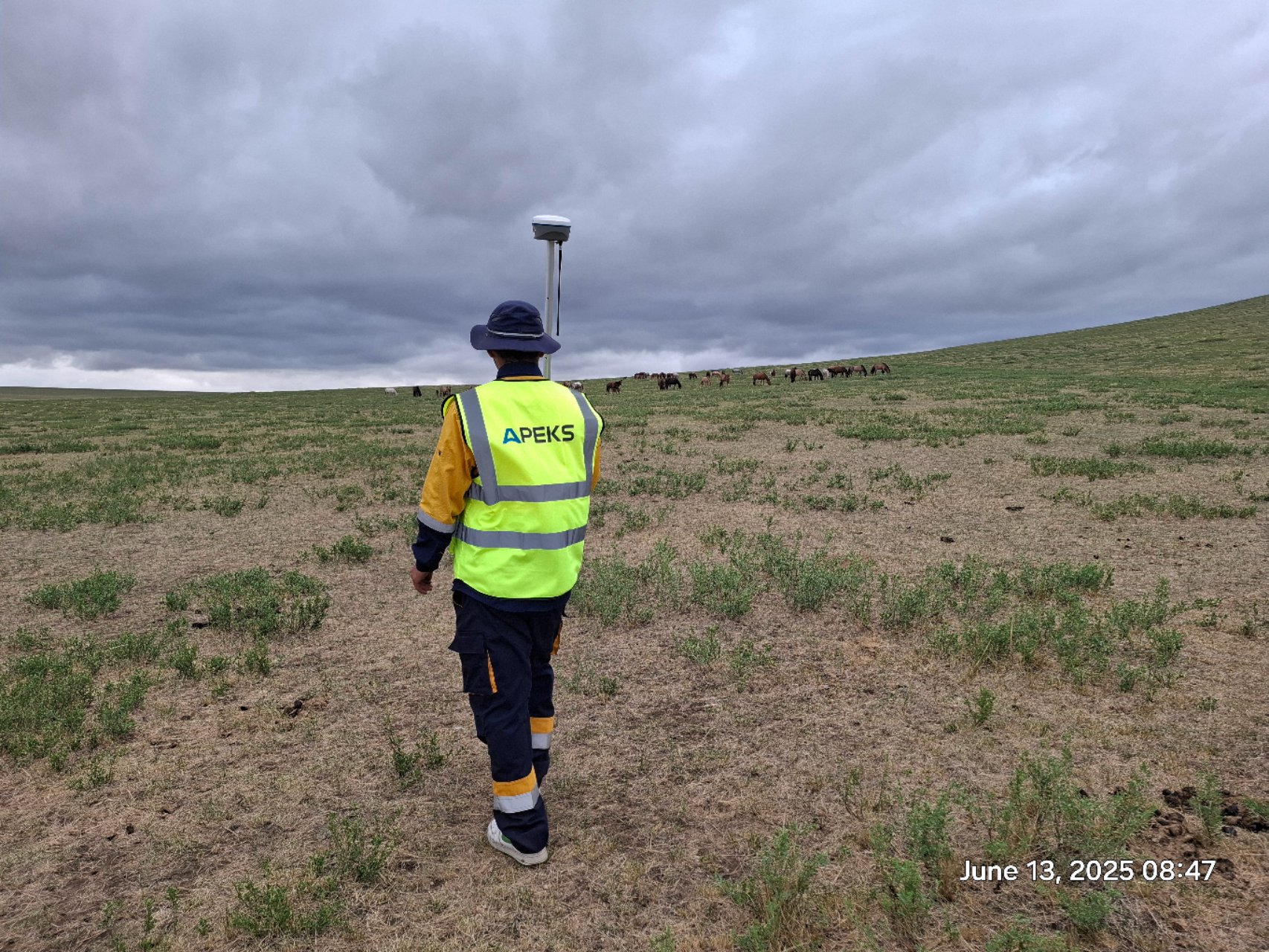 A surveyor carrying an APEKS RTK GNSS rover pole across the vast open grasslands of Mongolia