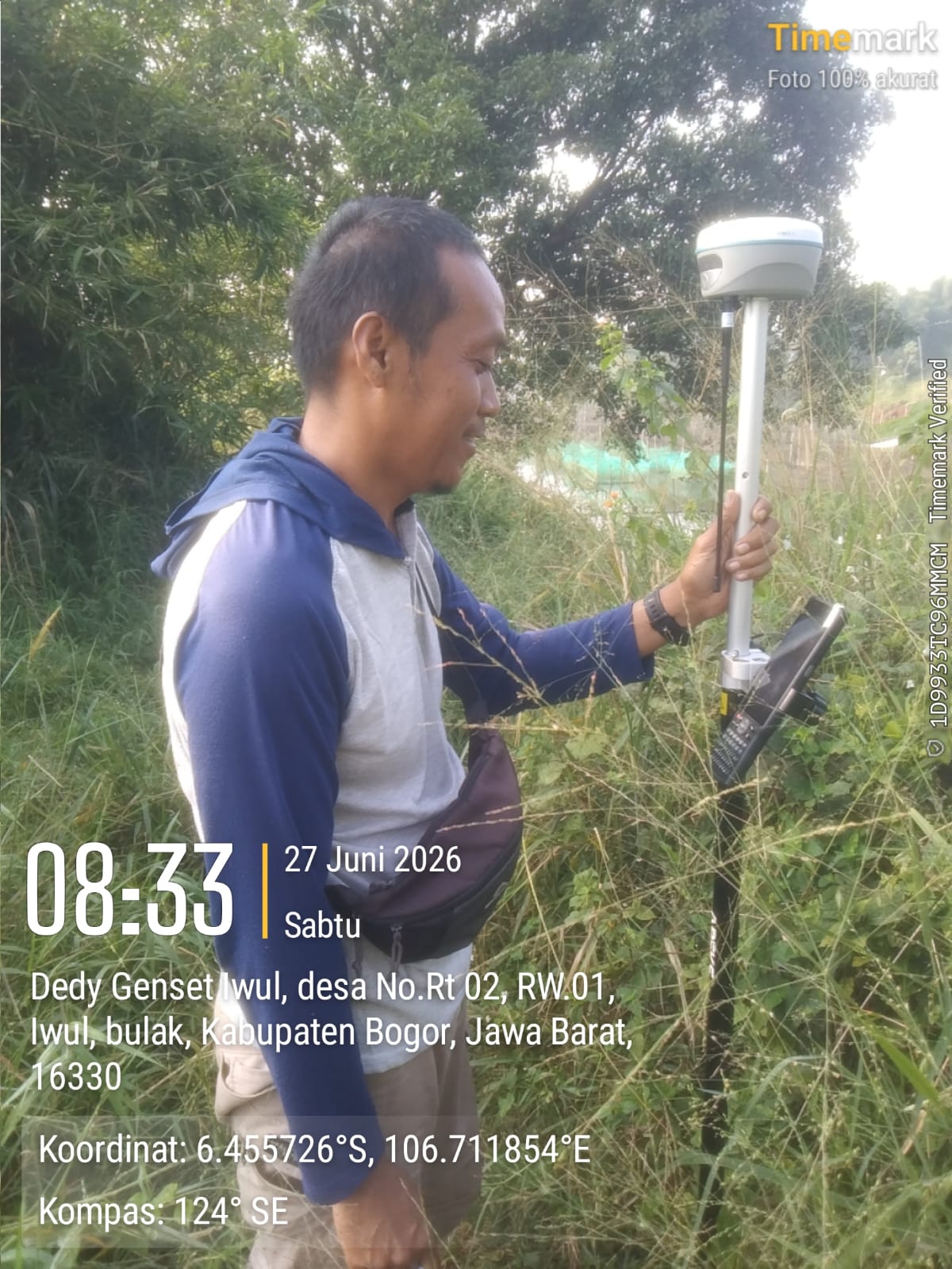 Local surveyor holding an APEKS RTK GNSS rover pole inside dense tropical vegetation in West Java, Indonesia